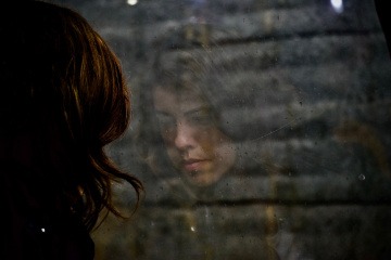 Eine Frau betrachtet ihr Spiegelbild im Fenster. Sie wirkt traurig und ratlos, vielleicht fragt sie sich: bin ich gut genug?