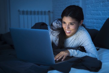 Eine Frau sitzt beim Laptop und blaues Licht erhellt den ganzen Raum