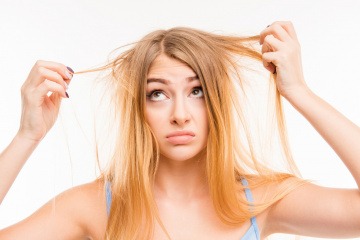 Eine Frau hält Strähnen ihrer blonden Haare in der Hand und schaut verzweifelt. Die Haare sehen sehr trocken aus.