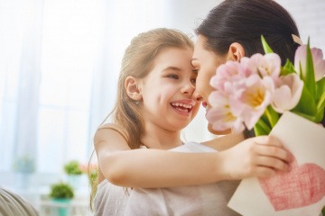 Eine Mädchen überreicht ihrer Mama Blumen und eine Grußkarte