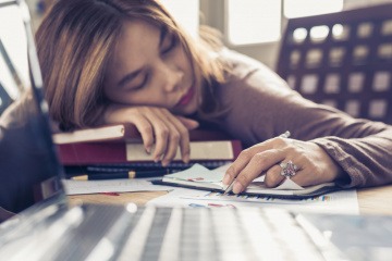 Eine Frau liegt am Schreibtisch wegen Burnout