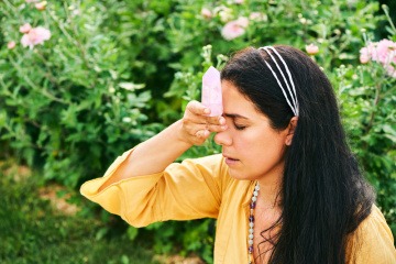 Eine Frau hält sich ein Mineral gegen Kopfschmerzen an die Stirn