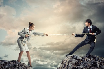 Egoismus in der Partnerschaft - Mann und Frau beim Tauziehen, jeder steht auf einem Felsvorsprung.