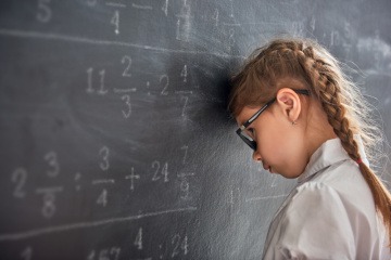 Frustriertes Mädchen lehnt mit Kopf an einer Schiefertafel.