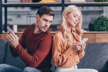 Ein junges Paar sitzt auf der Couch mit dem Handy in ihrer Handy