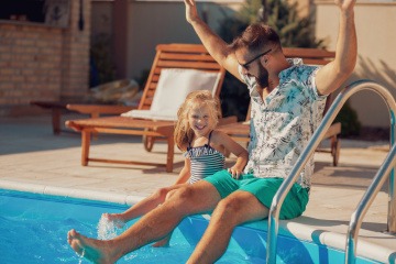 Kind und Mann sitzen am Pool-Rand und halten die Füße ins Wasser