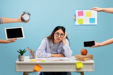 Frau wird mit Anfragen und Aufgaben bei der Arbeit überhäuft und wirkt verzweifelt.