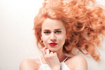 Eine Frau im Freien mit welligen erdbeerblonden Haaren trägt einen roten Lippenstift