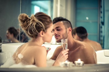 Ein Mann und eine Frau sitzen mit einem Glas in der Badewanne und küssen sich