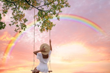 Frau auf Schaukel vor Regenbogen