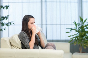 Eine Frau sitzt mit Erkältung auf einer Couch