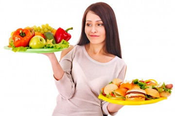 Eine Frau hält ein Teller gesunde Ernährung und ein Teller Burger in der Hand