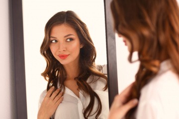 Eine Frau steht vor dem Spiegel und betrachtet ihre Haare