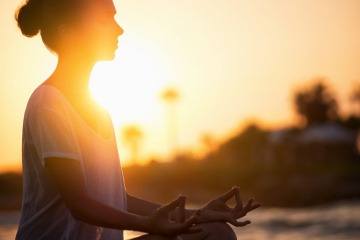 Eine Frau meditiert bei Sonnenuntergang am Strand