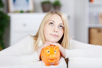 Eine Frau liegt mit einem Sparschwein auf der Couch