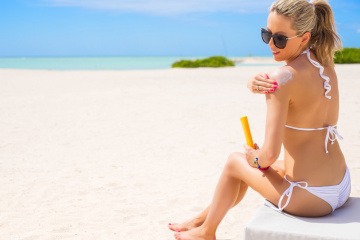 Eine Frau sitzt am Strand und gibt Sonnenschutz auf Ihre Schulter