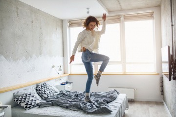 Eine Frau tanzt auf ihrem Bett