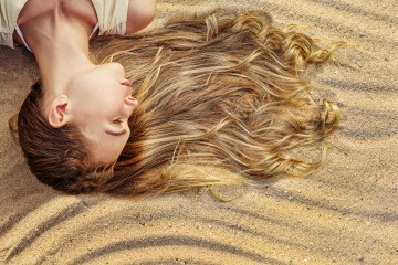 Eine Frau liegt mit ihrer Frisur am Sandstrand im Sommer