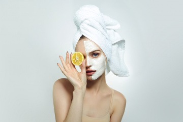 Frau mit Creme im Gesicht und Zitrone in der Hand