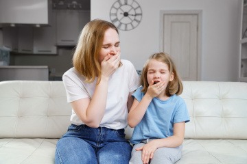 Mutter und Tochter sitzen und gähnen gemeinsam auf der Couch 