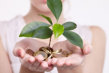 Eine Frau hält Münzen in der Hand, aus denen eine Pflanze wächst