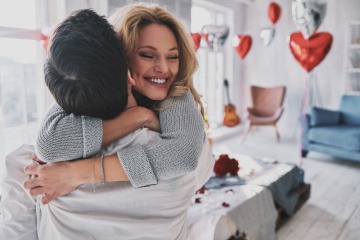 Frau umarmt erfreut einen Mann, im Hintergrund Herzluftballons