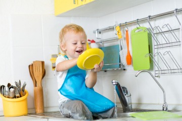 Kleines Kind spielt Geschirr abspülen in einer Spielzeugküche.