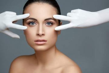 Zwei Hände in Handschuhen bei den Augen als Zeichen für Augenlidkorrektur