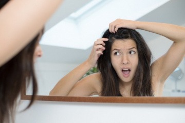 Eine Frau betrachtet im Spiegel ihren Haarausfall