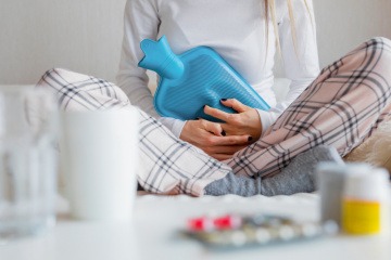 Frau mit Wärmflasche auf dem Bauch.