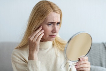 Eine Frau betrachtet ihre Hautausschläge im Gesicht