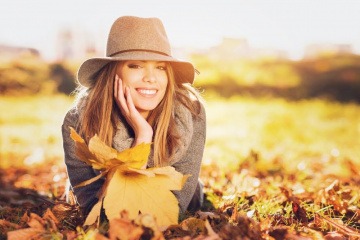 Eine Frau liegt auf einer mit Laub bedeckten Wiese und lächelt in die Kamera. Sie weiß anscheinend sehr genau, wie sie den Herbst genießen kann.