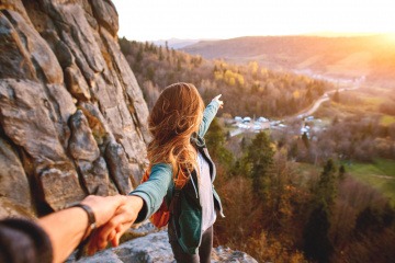 Horizont erweitern - junges Paar beim Wandern auf einem Berg, die Frau zeigt in Richtung Horizont.