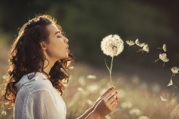 Eine Frau lebt im Moment und genießt das Sein. Sie bläst eine Pusteblume