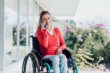 Eine Frau sitzt im Rollstuhl und telefoniert glücklich