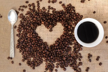 Neben einer Kaffeetasse liegen Kaffeebohnen und ein Löffel