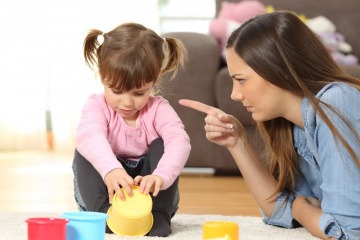Eine Mutter ermahnt ihr spielendes Kleinkind mit erhobenem Zeigefinger. 