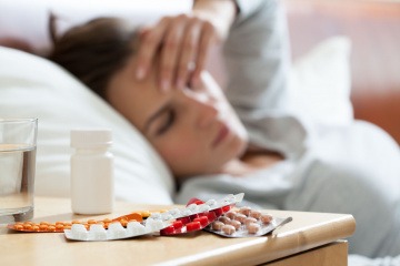 Eine Frau mit Krankheit liegt im Bett mit Tabletten daneben