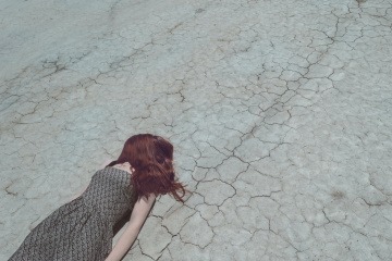 Eine Frau, die ihren Lebenssinn verloren hat, liegt auf einem ausgetrockneten Wüstenweg.