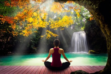 Eine Frau sitzt in einer herbstlichen Landschaft und macht Yoga