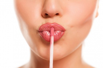 Frau macht einen Kussmund und hält einen Lipgloss an die Lippen