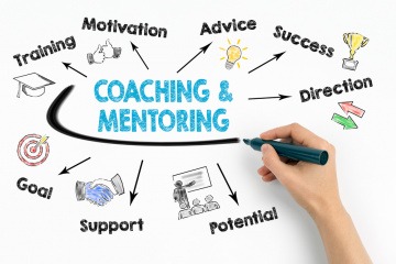 Auf ein Schild werden Schlagworte für Coaching und Mentoring geschrieben