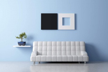 Das Thema minimalistisch Wohnen wird in diesem Bild beispielhaft anhand eines Raums gezeigt, in dem die Einrichtung nur aus einem Sofa, einem Regal mit einer Topfpflanze und einem Bild an der Wand gibt. Der Raum wirkt dennoch einladend und gemütlich.