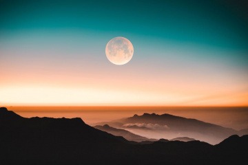 Im Hintergrund einer Berglandschaft befindet sich der Mond