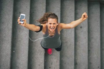 Eine Frau joggt durch den Park. Hinter ihr geht die Sonne auf. Sie wirkt glücklich und motiviert.