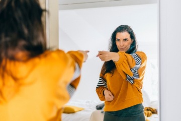 Frau motiviert sich mit positiven Selbstgesprächen vor einem Spiegel.