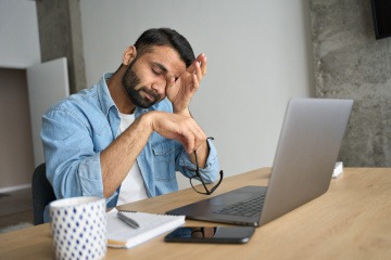 Mann am Schreibtisch reibt sich die Augen