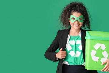 Frau gekleidet als Öko-Superheld mit Mülltonne auf grünem Hintergrund.