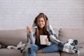 Nach Trennung glücklich werden - junge Frau sitzt auf dem Sofa, weint und isst dabei Eis aus einem riesigen Becher.