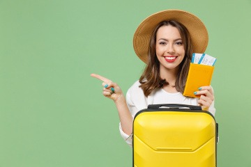Nachhaltig reisen - junge lächelnde Frau mit gepacktem Koffer und zwei Flugtickets in der Hand. 